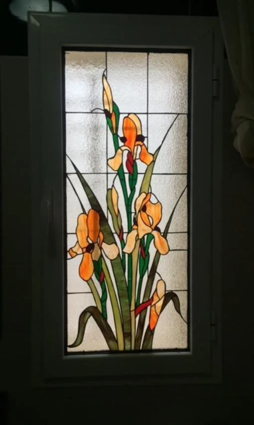 Vitrail vertical avec fleurs orangées, feuilles vertes et fond clair texturé.